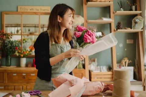 Seseorang sedang merangkai buket bunga segar di studio usaha florist rumahan