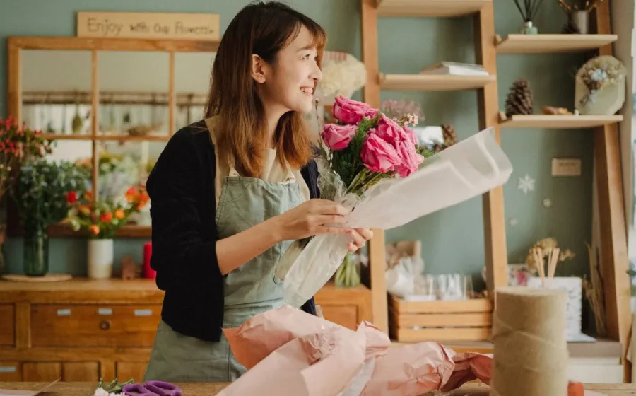 Seseorang sedang merangkai buket bunga segar di studio usaha florist rumahan