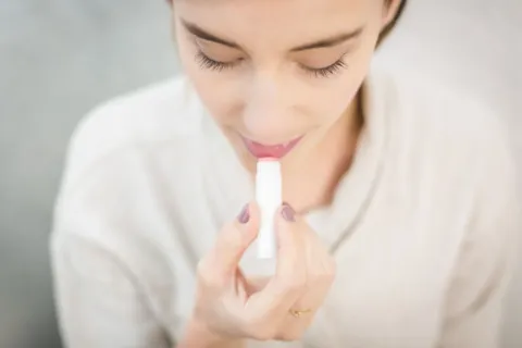 Seseorang mengoleskan lip balm pelembap untuk mempraktikkan cara mengatasi bibir kering