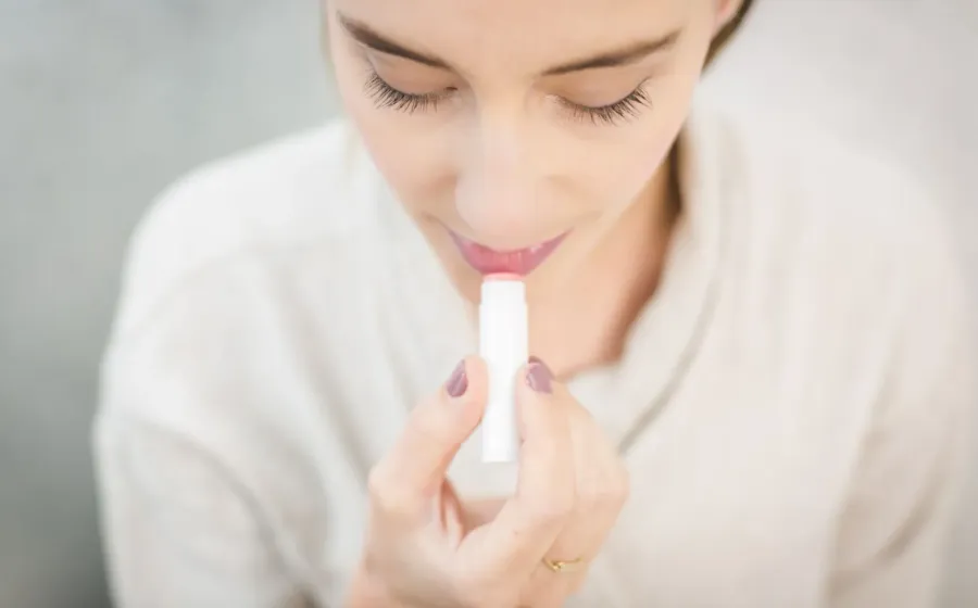 Seseorang mengoleskan lip balm pelembap untuk mempraktikkan cara mengatasi bibir kering