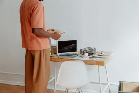Seseorang menerapkan kebiasaan menjaga postur tubuh yang baik saat duduk di meja kerja depan laptop