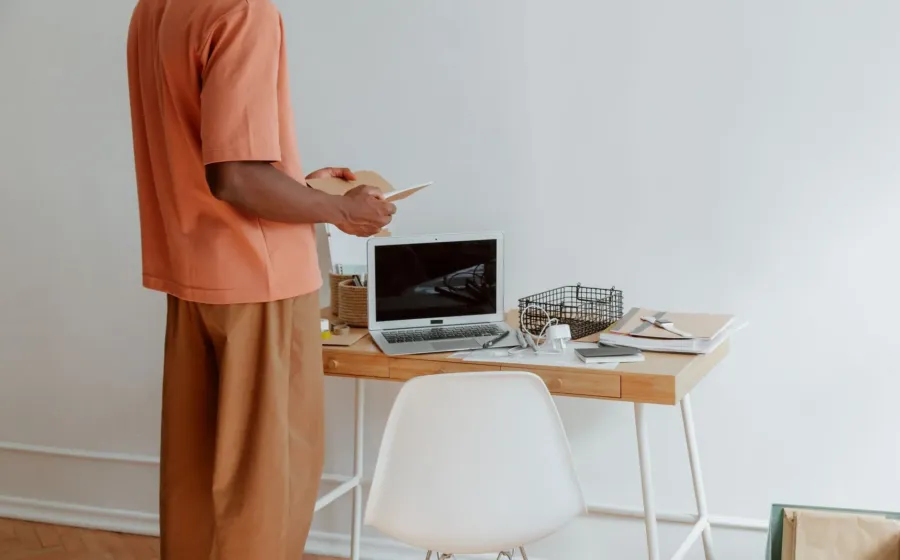 Seseorang menerapkan kebiasaan menjaga postur tubuh yang baik saat duduk di meja kerja depan laptop