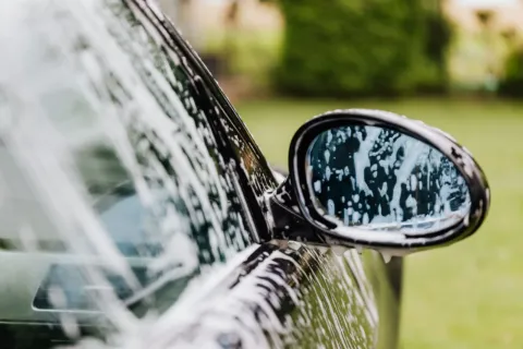 Seseorang sedang mengelap kaca spion mobil dengan kain mikrofiber halus