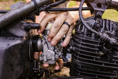 Perawatan karburator motor klasik menggunakan obeng untuk membersihkan mangkok karburator