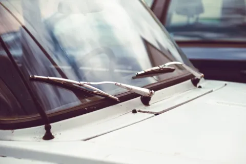 Pemilik mobil sedang membersihkan karet wiper mobil memakai kain mikrofiber basah
